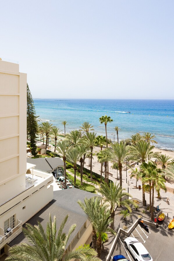 A beachfront hotel with a view of the ocean, palm trees, and a parking area.
