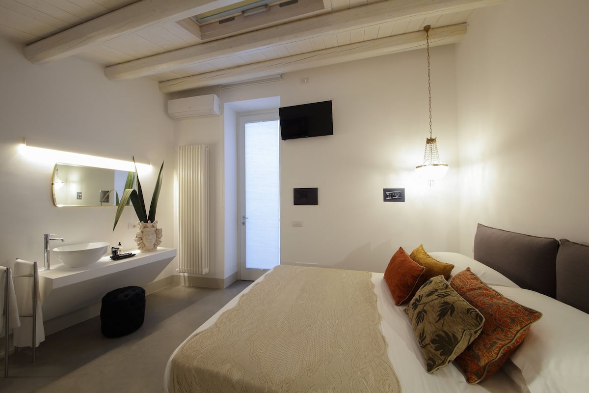 Ein modernes Schlafzimmer mit einem großen Bett, einem Nachttisch, einem integrierten Waschbecken und einem großen Spiegel.