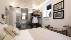 Une chambre moderne avec un grand lit, une armoire intégrée, une petite table avec un téléphone et une fenêtre ornée d’œuvres d’art.