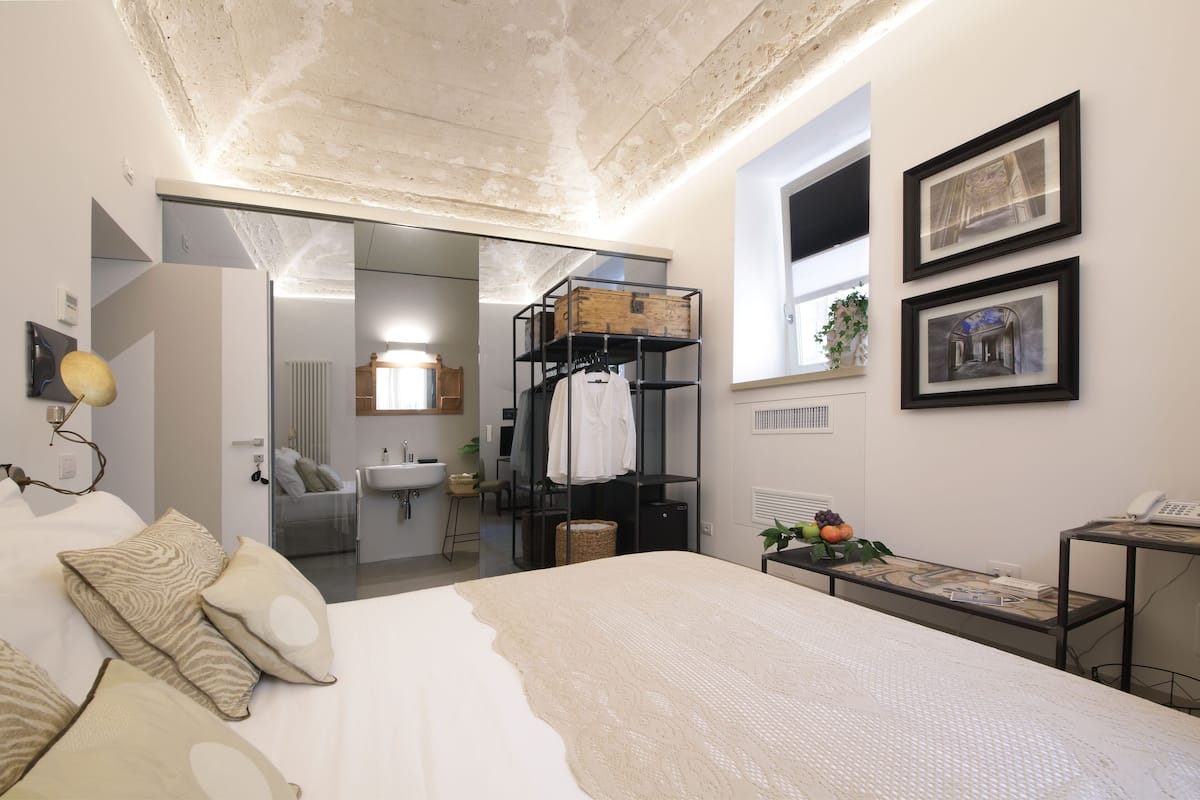 Ein modernes Schlafzimmer mit einem großen Bett, einem Einbauschrank, einem kleinen Tisch mit Telefon und einem Fenster mit Kunstwerk.