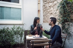 Two people sitting at a table with a bottle of wine, a plate of food, and a window in the background.