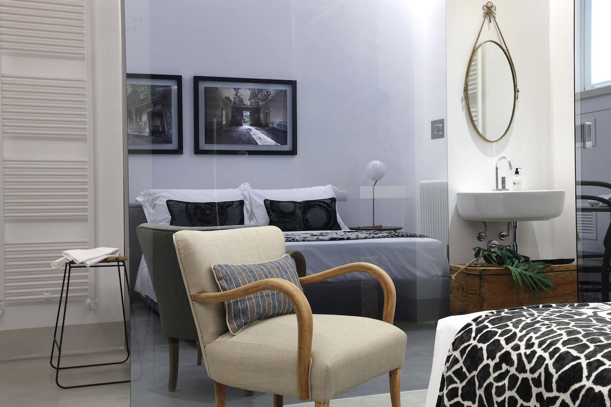 Ein modernes Schlafzimmer mit einem Bett, einem Sessel, einem kleinen Tisch, einem Spiegel und einem Wandbild.