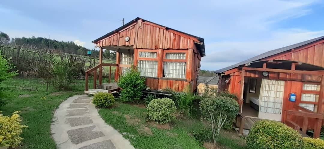 A rustic wooden house with a porch, a stone pathway, and a fenced garden.