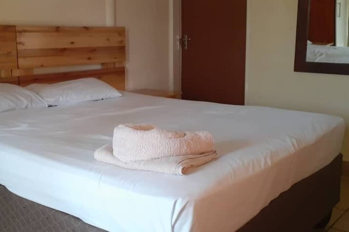 A neatly made bed with a wooden headboard, a folded towel on the bed, and a wooden nightstand beside it.