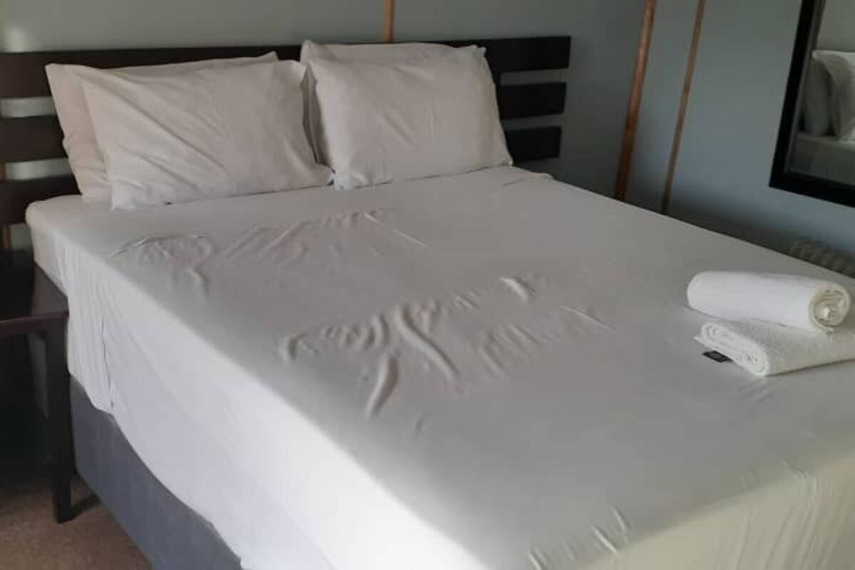 A neatly made bed with white linens, a wooden nightstand, and a folded towel on the bed.