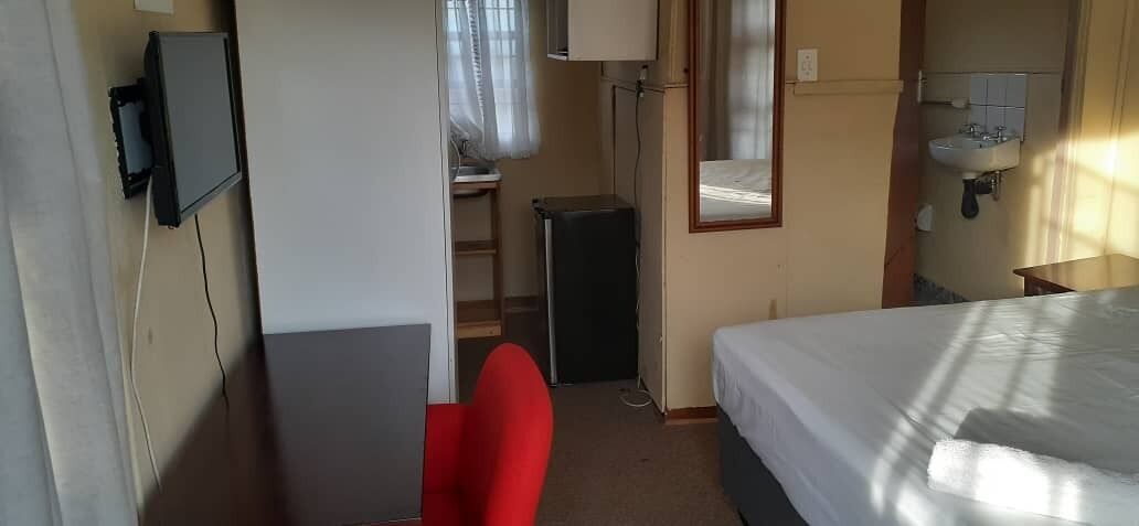 A hotel room with a bed, a desk with a chair, a TV, a small cabinet, and a window with curtains.