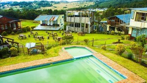 A swimming pool with a brick border, surrounded by picnic tables and a grassy area.