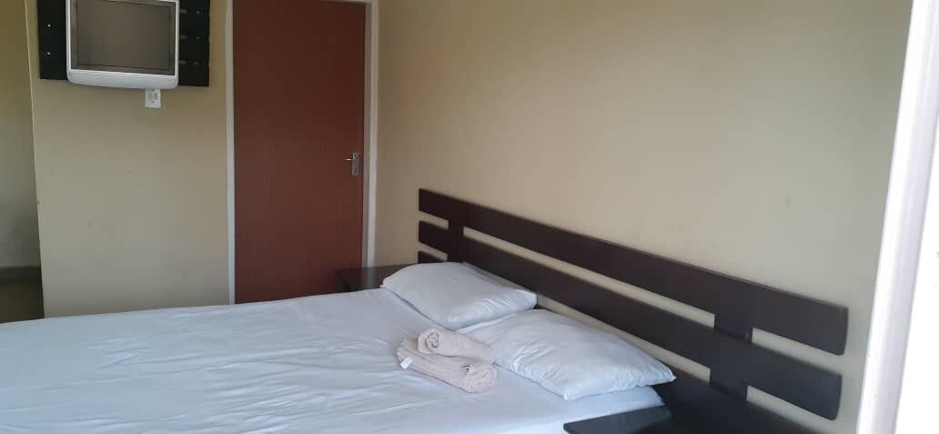A neatly made bed with pillows and a folded towel, a television mounted on the wall, and a door to the side.