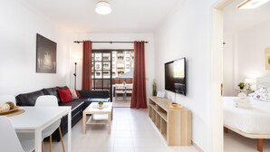 Een moderne woonkamer met een bank, eettafel, televisie en uitzicht door grote ramen.