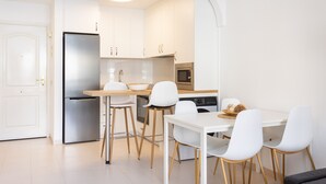 Een moderne keuken met witte kastjes, roestvrijstalen apparatuur en een eethoek met witte stoelen en een houten tafel.