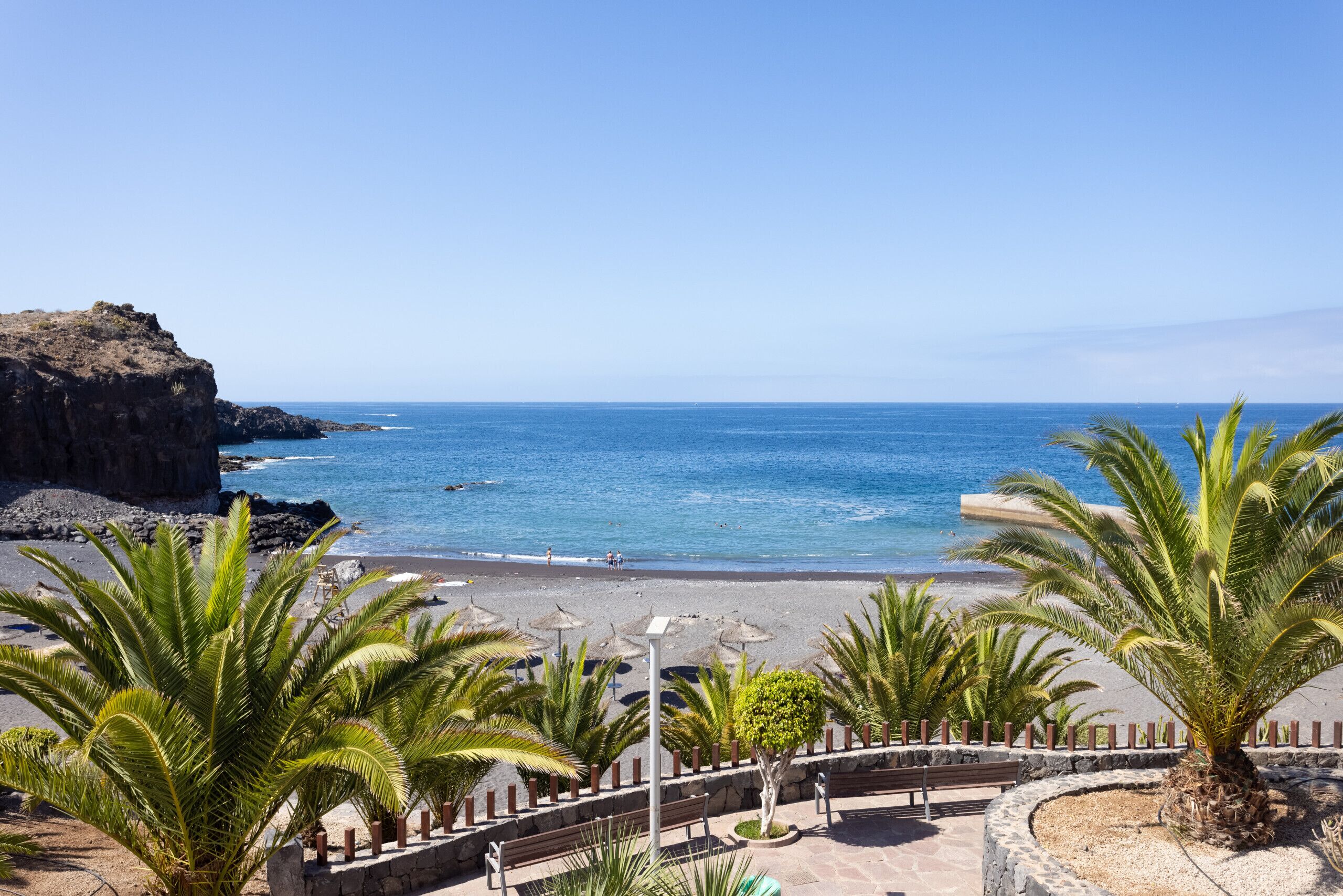 A beach with palm trees, a rocky cliff, and a clear blue sky.