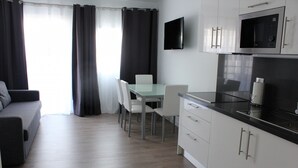 A modern kitchen with white cabinets, a black countertop, and a built-in microwave. There is a dining area with a glass table and white chairs.