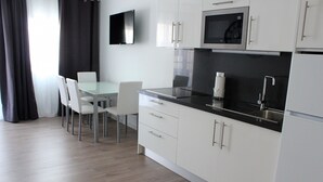A modern kitchen with white cabinets, a black countertop, and stainless steel appliances. There is a dining table with chairs.