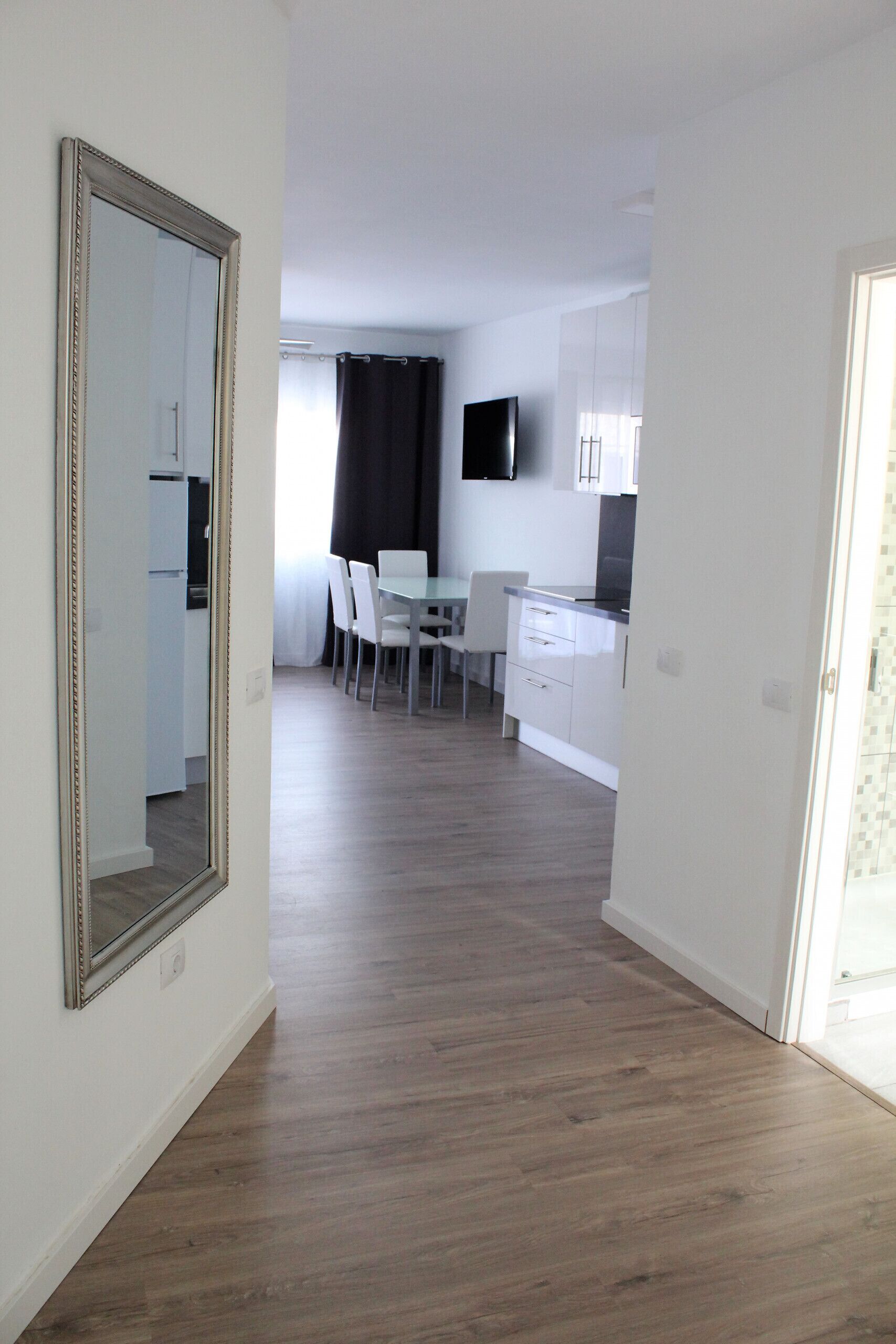 A modern kitchen with white cabinets, a flat-screen TV, and a dining area with chairs and a table.