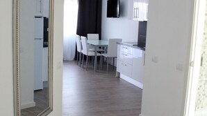 A modern kitchen with white cabinets, a flat-screen TV, and a dining area with chairs and a table.