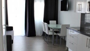 A modern kitchen with white cabinets, a flat-screen TV, and a dining area with a table and chairs.