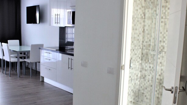 A modern kitchen with white cabinets, a dining table with chairs, and a glass shower enclosure.