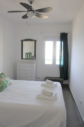 A bedroom with a bed, a dresser, a ceiling fan, a window with curtains, and a mirror.