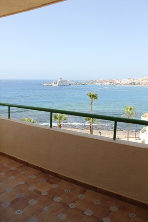 A balcony with a view of the sea, a ship, and a beach with palm trees.