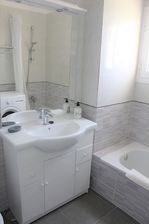 Une salle de bain moderne avec un double vasque, une baignoire et un lave-linge.