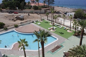 A resort with a swimming pool, lounge chairs, and a beach view.