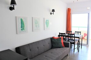 A modern living room with a grey sofa, a dining table with chairs, and three framed botanical prints on the wall.