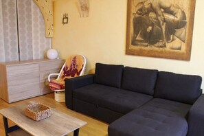 A living room with a dark sofa, a wooden coffee table, a patterned chair, a white cabinet, and a painting on the wall.
