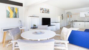 A modern living room with a round white table, wicker chairs, and a blue sofa. There is a kitchen area with white cabinets and a dining table. - Tranquilidad, playa y vistas al mar (Callao Salvaje)