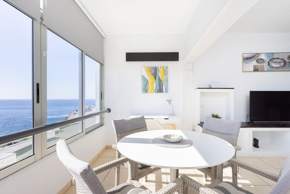 A balcony with a white table and wicker chairs, overlooking the sea.
