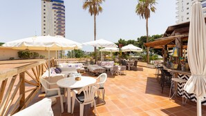 An outdoor patio area with white tables and chairs, umbrellas, and a bar area.