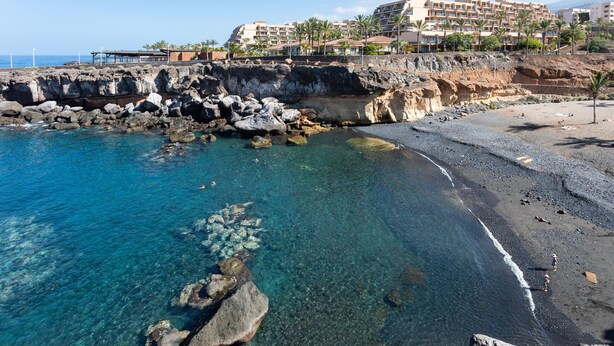 A coastal hotel with a rocky beach, clear blue waters, and a view of the sea.