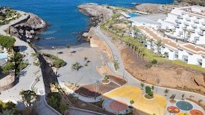 An aerial view of a coastal resort with a beach, palm trees, and a white building complex.