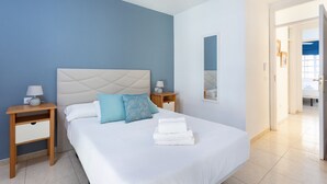 Un dormitorio con una cama, dos mesitas de noche, un tocador y una puerta de baño.