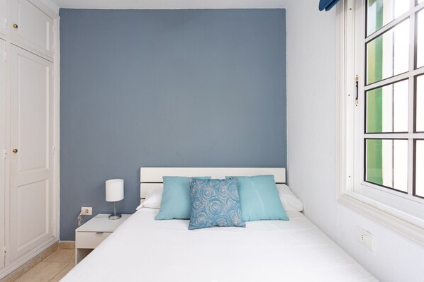 A bedroom with a bed, a nightstand, a lamp, and a window with green blinds.