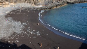 Una playa con acantilados rocosos, agua azul cristalina y gente dispersa.