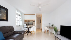 Una sala de estar moderna con un sofá de cuero marrón, un comedor con sillas blancas, una cocina con armarios blancos y un televisor de pantalla plana sobre un soporte.