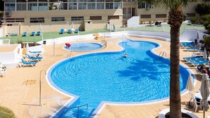 A large pool with a palm tree, lounge chairs, and a building in the background. - Fabuloso apartamento con magnificas vistas al mar (Callao Salvaje)