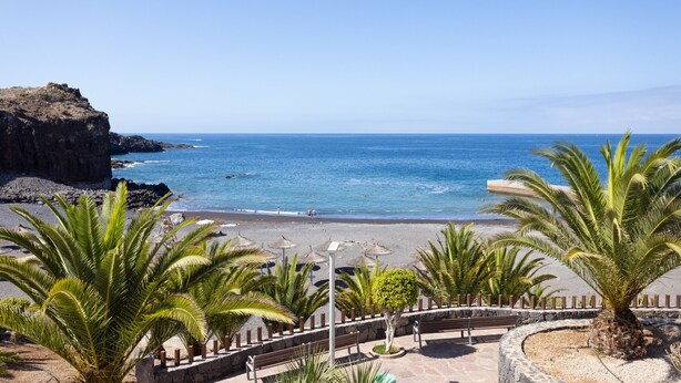 A beach with palm trees, a rocky cliff, and a clear blue sky. - Fabuloso apartamento con magnificas vistas al mar (Callao Salvaje)