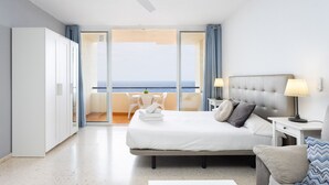 Una habitación de hotel con cama, mesitas de noche, sofá, balcón con vistas y armario.