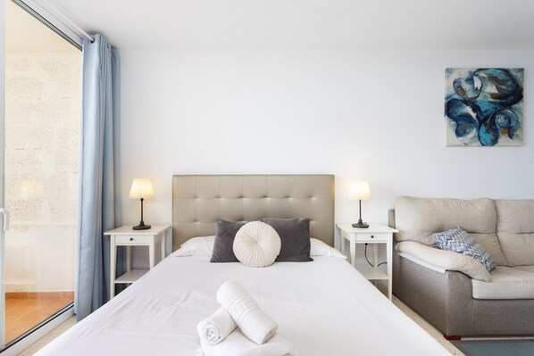Ein Hotelzimmer mit einem großen Bett, zwei Nachttischen mit Lampen, einem grauen Sofa und einem Bild an der Wand.