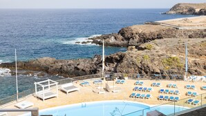 Zona de piscina con sillones de descanso y vista al océano.