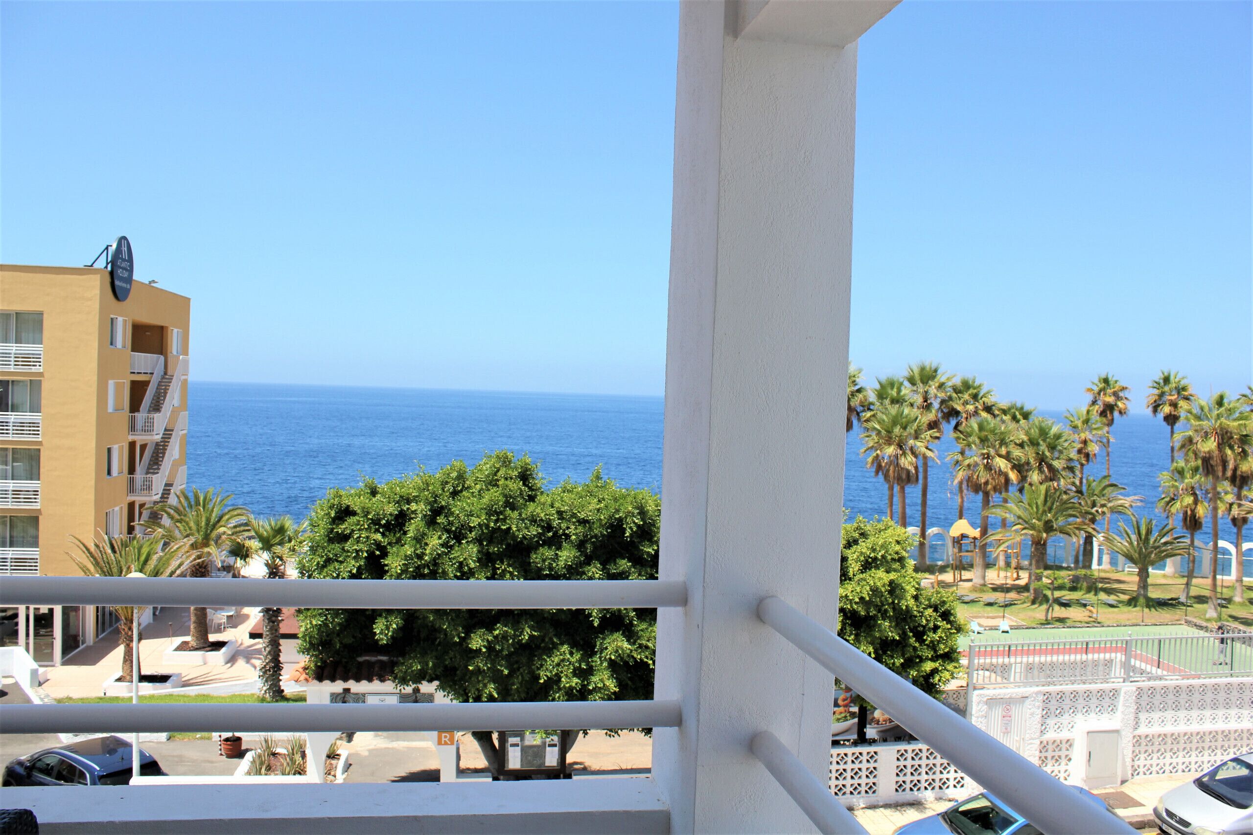 A balcony with a view of the sea and palm trees.
