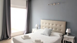 Un lit bien fait, avec du linge de lit blanc et deux oreillers, une table de chevet avec une lampe et une fenêtre avec des rideaux.