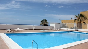 Une piscine rectangulaire avec un escalier en métal, entourée de chaises longues blanches et d’une clôture blanche.