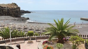 Une plage avec des parasols, des chaises longues et une falaise rocheuse.