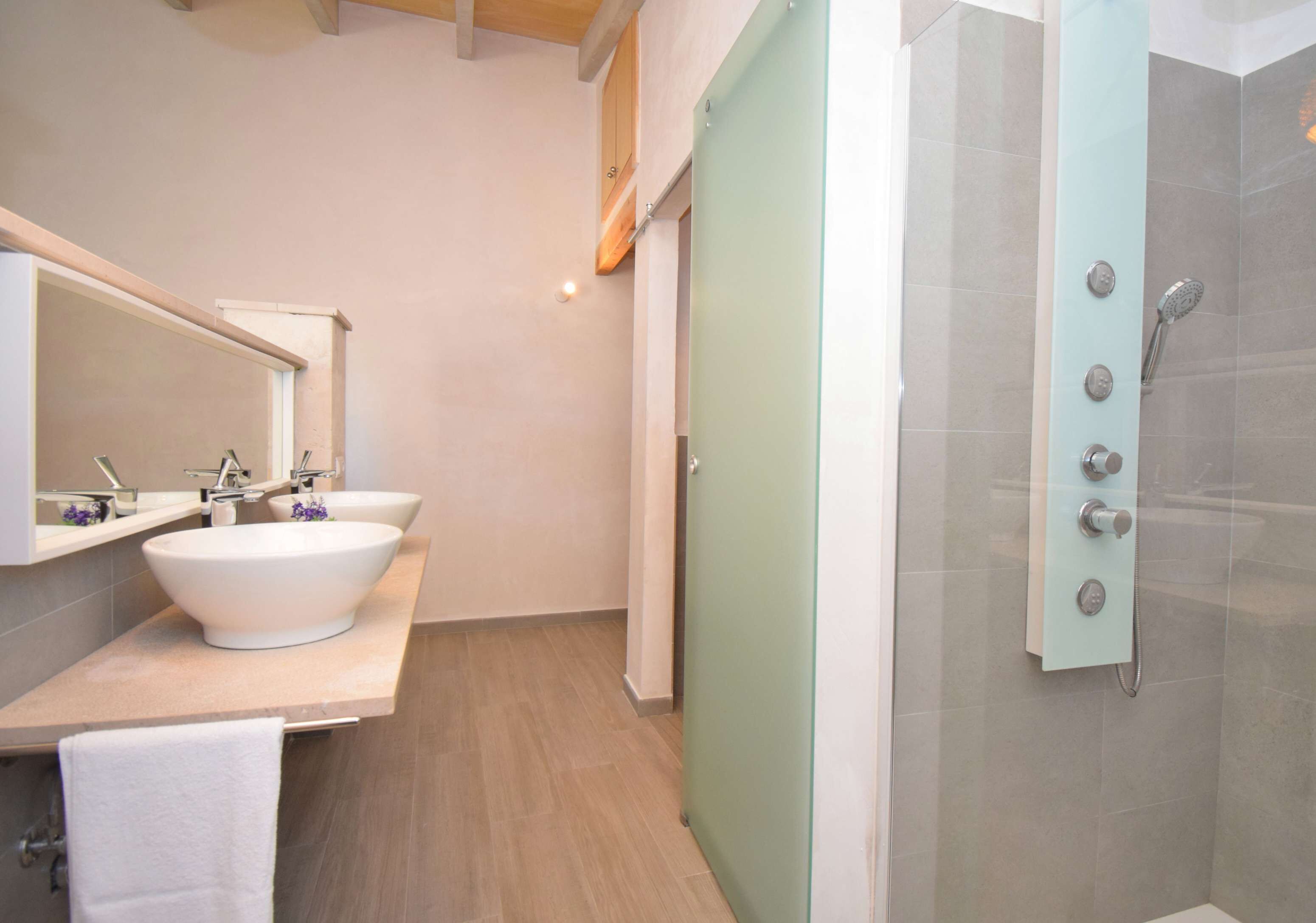 A modern bathroom with a large white sink, a mirror, and a shower with multiple controls.
