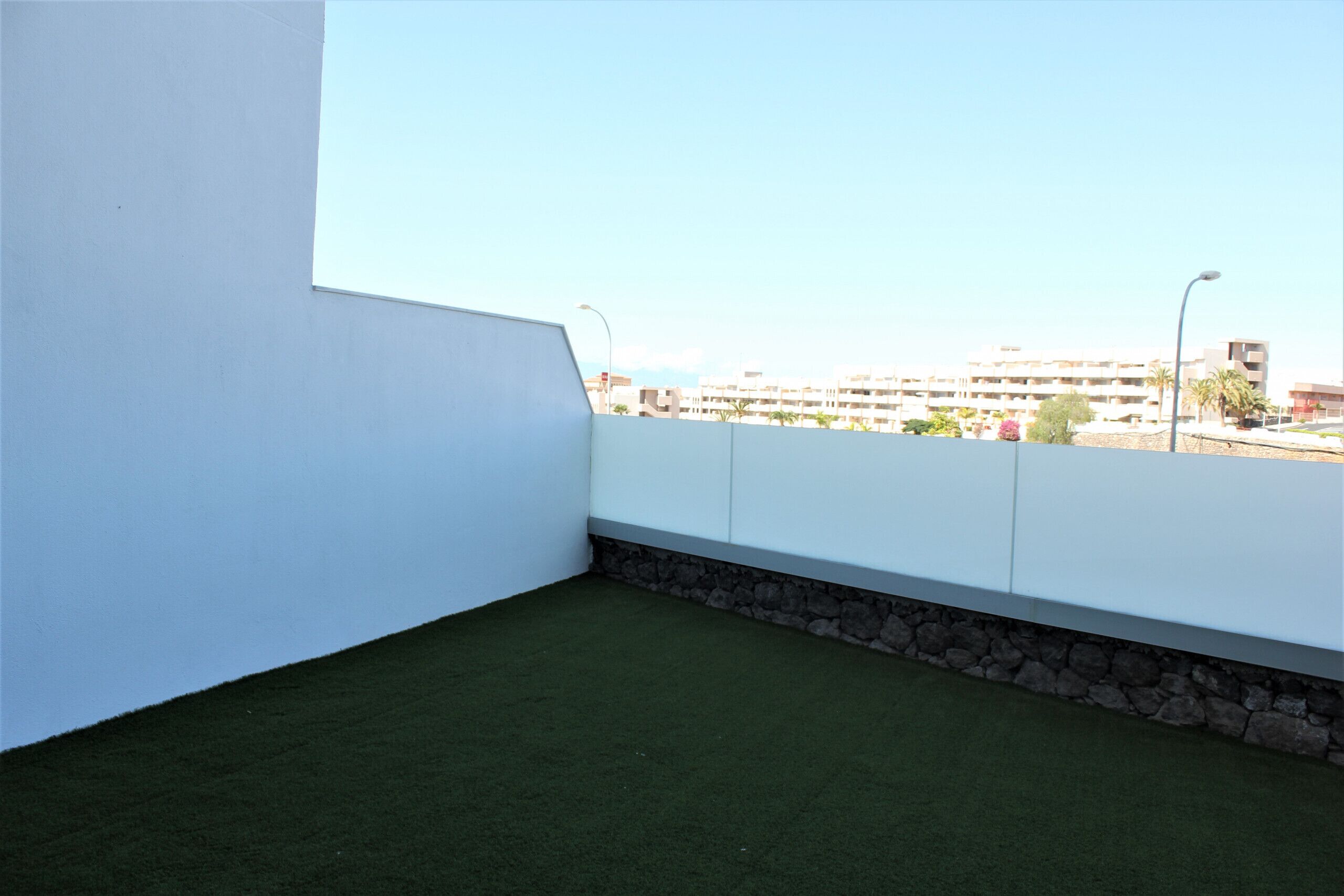 A rooftop terrace with a green artificial lawn, white walls, and a stone base.