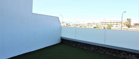 A rooftop terrace with a green artificial lawn, white walls, and a stone base.
