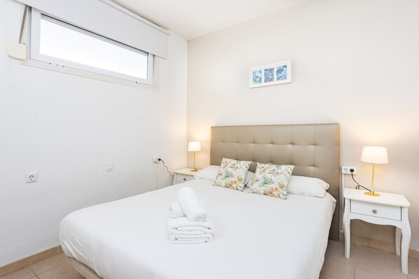 Un dormitorio con una cama, dos mesitas de noche, una ventana y un cuadro colgado en la pared.