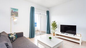 Ein modernes Wohnzimmer mit Sofa, Couchtisch, Fernseher und einer Schiebeglastür, die auf einen Balkon führt.